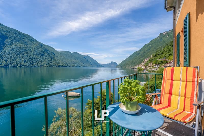 Balcony overlooking a scenic lake surrounded by mountains, with colorful patio furniture and potted plants