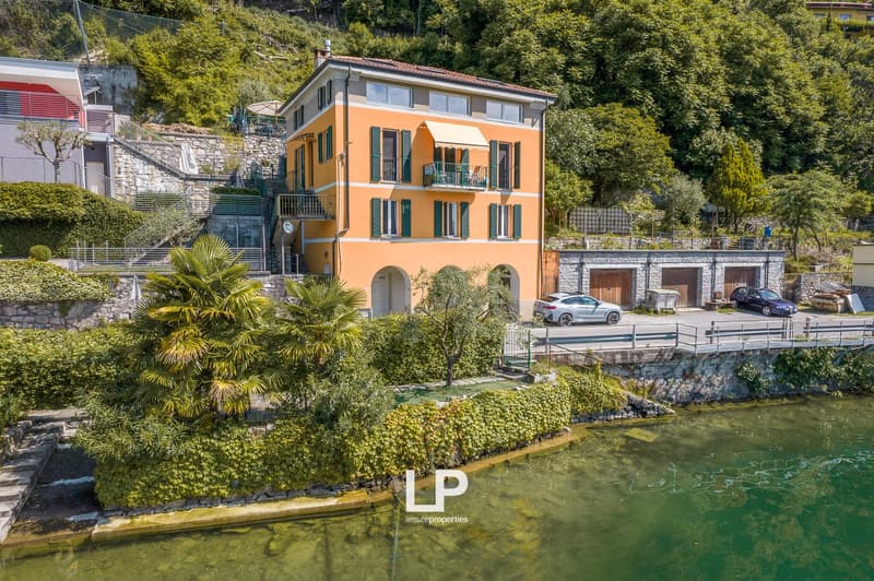 3-story orange building with balconies, surrounded by lush greenery and a small body of water, with parking spaces in front