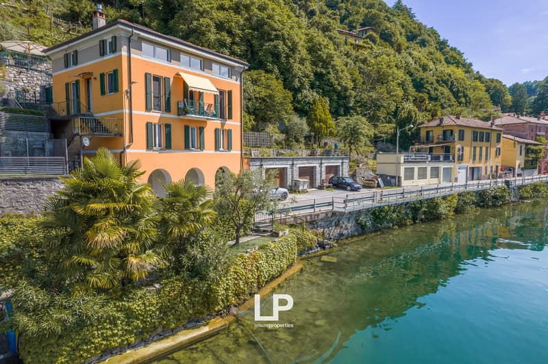 3-story orange building with balconies, surrounded by lush greenery and a river, located in a scenic mountainous area