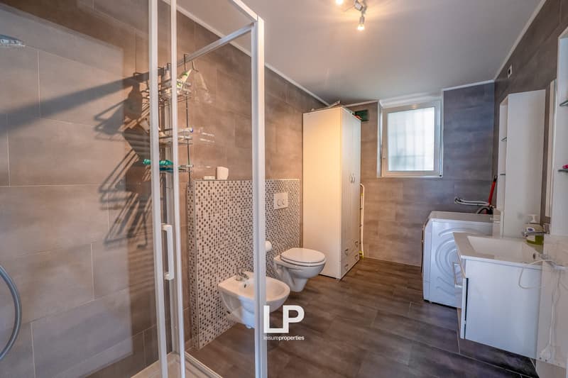 Spacious bathroom with tiled walls, shower enclosure, toilet, bidet, and a washing machine
