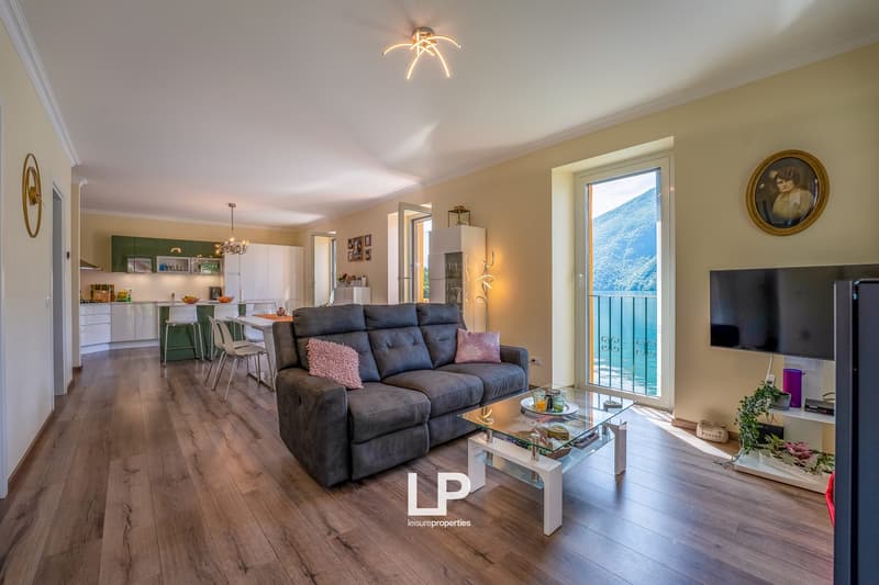 Open-concept living room and kitchen, hardwood floors, gray sofa, glass coffee table, wall-mounted TV, balcony with scenic view