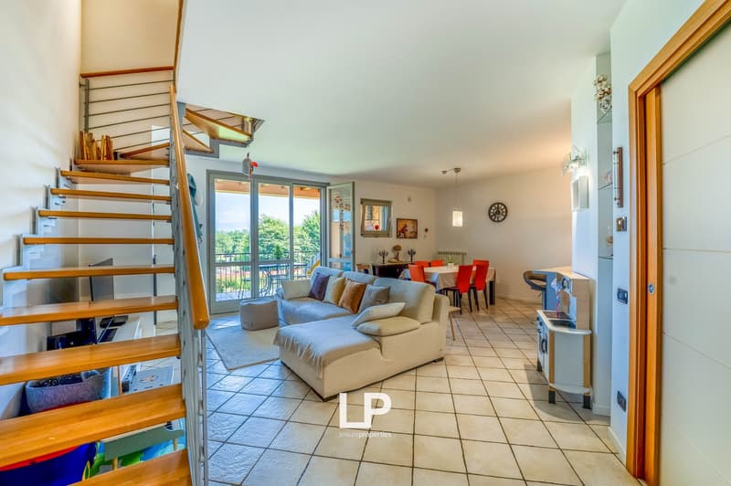 Open-concept living room and dining area, hardwood stairs, large windows, beige sofa, red dining chairs, tiled flooring, balcony access