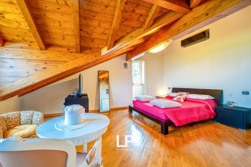 Spacious bedroom with wooden beamed ceiling, hardwood floors, large bed with pink bedding, dresser, and a small round table with a cake on it.