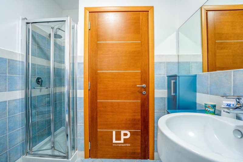Bathroom with glass shower enclosure, wooden door with 'LP' logo, blue and white tiled walls, and a bathtub