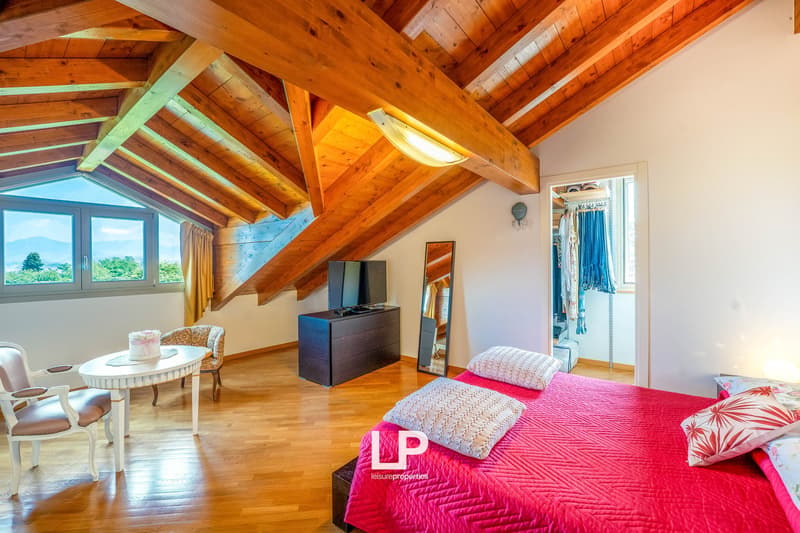 Spacious attic bedroom with wooden beamed ceiling, large windows, hardwood floors, TV stand, and a cozy seating area with a round table