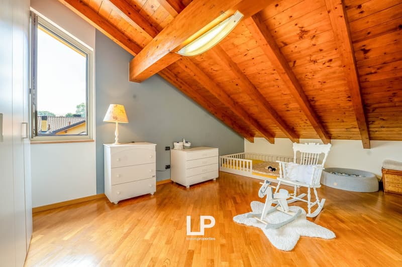 Spacious bedroom with wooden vaulted ceiling, hardwood flooring, white dresser and crib, rocking chair, and large window providing natural light