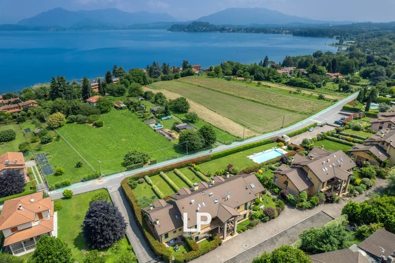 Aerial view of a residential area with houses, gardens, and a swimming pool overlooking a large lake surrounded by mountains