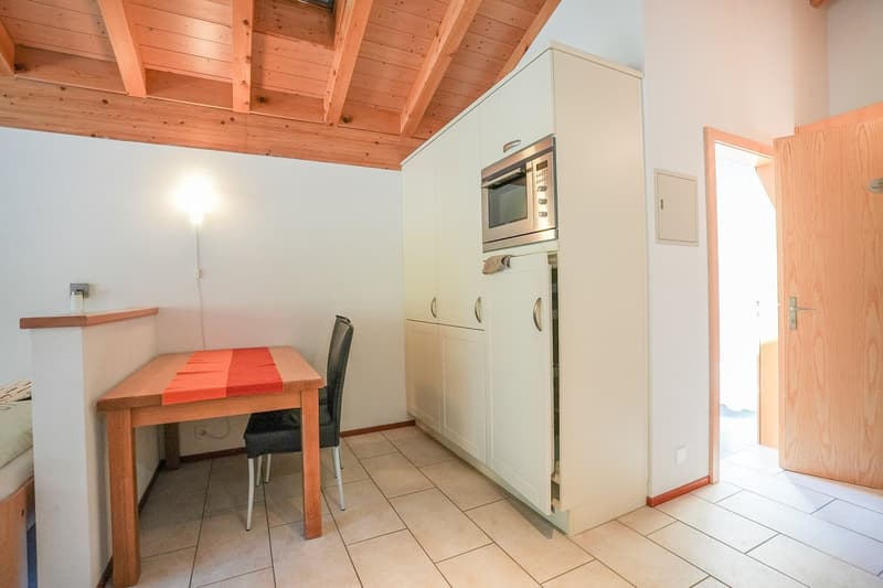 Wooden ceiling, white walls, tiled floor, kitchen cabinets, oven, dining table with chairs