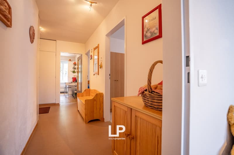 Hallway with wooden furniture, shelves, and decor. Doors leading to other rooms. Warm lighting and neutral color scheme.
