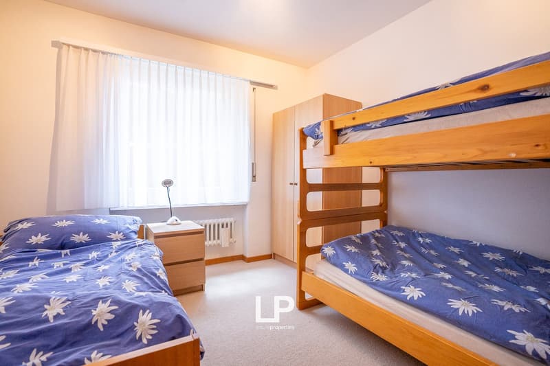 Bedroom with bunk beds, wooden furniture, blue and white floral bedding, curtains, and a small table lamp