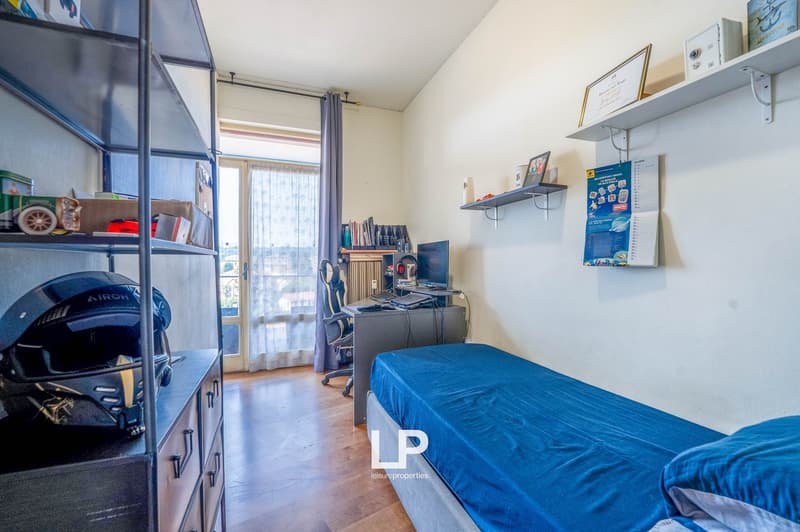 Bedroom with blue bedding, shelving unit, desk with computer, and balcony access