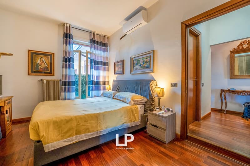 Spacious bedroom with hardwood floors, large windows, blue and yellow bedding, wooden furniture, and artwork on the walls.