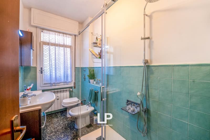 Bathroom with blue tile walls, toilet, bidet, sink, and shower with curtain rod
