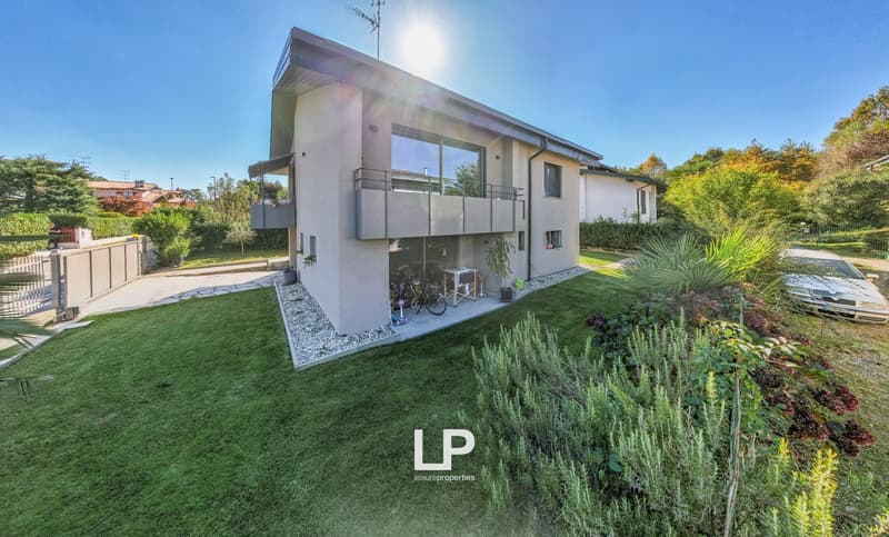 Two story house, large windows, balcony, paved driveway, landscaped garden