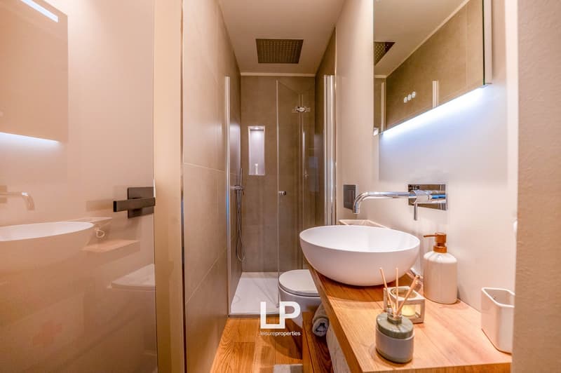 Modern bathroom with a white vessel sink, wooden vanity, glass shower enclosure, and a toilet. The bathroom has a minimalist and contemporary design.