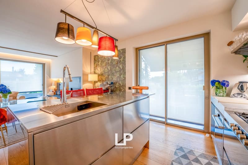 Modern kitchen with stainless steel appliances, stone backsplash, pendant lighting, and sliding glass doors leading to a balcony or terrace