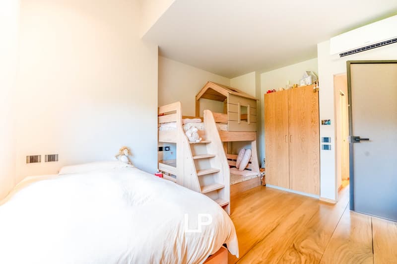 Spacious bedroom with a bunk bed, wooden wardrobe, and hardwood flooring. The room has a bright and airy feel with white walls and natural lighting.