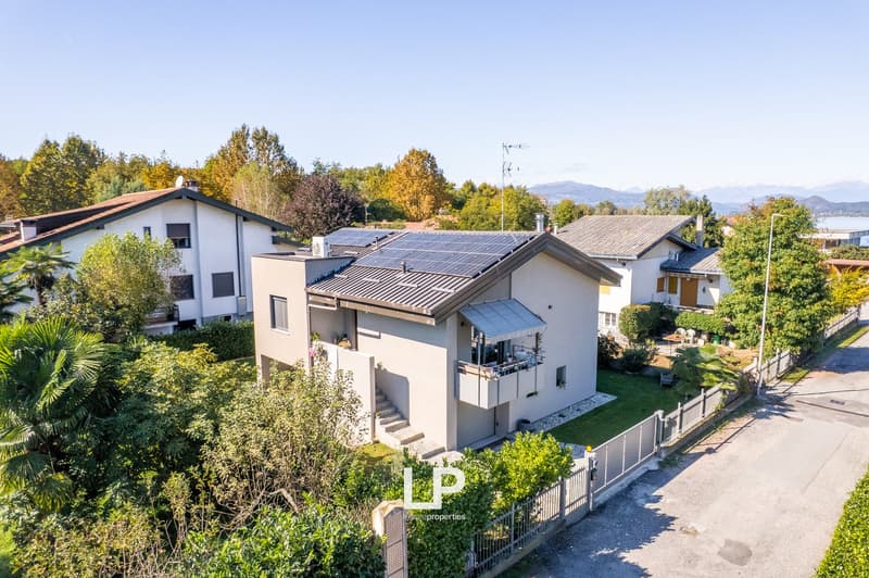2 story house, white walls, brown roof, solar panels on the roof, balcony on the upper floor, stairs to the entrance