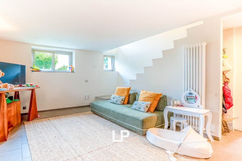 Spacious living room with large windows, green sofa with colorful pillows, white side table, TV stand, and radiator