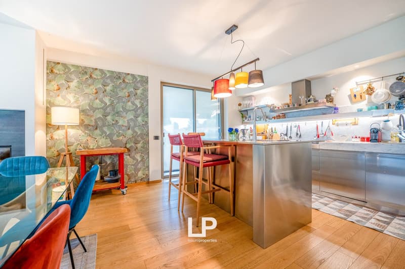 Open concept kitchen with stainless steel appliances, wooden bar stools, colorful patterned wallpaper, and a mix of modern and vintage decor elements.