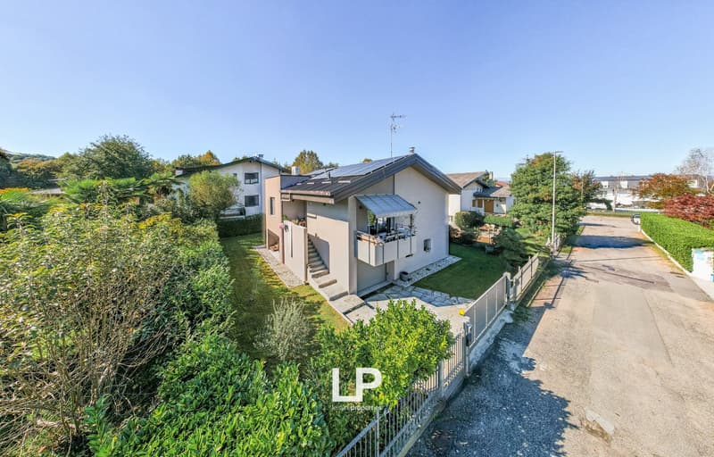 two-story house, red brick, solar panels, raised ground floor, gated driveway, garden, green trees
