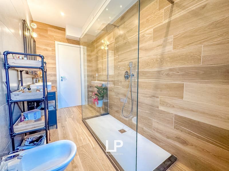 Spacious bathroom with wood-like tile walls and floors, glass shower enclosure, vanity, and storage shelving unit