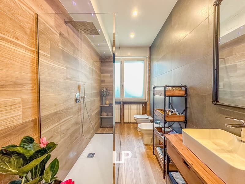 Spacious bathroom with wooden floor tiles, glass shower enclosure, vanity unit with sink, and a storage rack.
