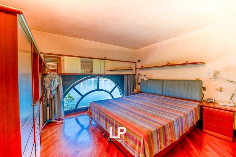 Spacious bedroom with large arched window, wooden floors, built-in cabinets, and a colorful striped bedspread