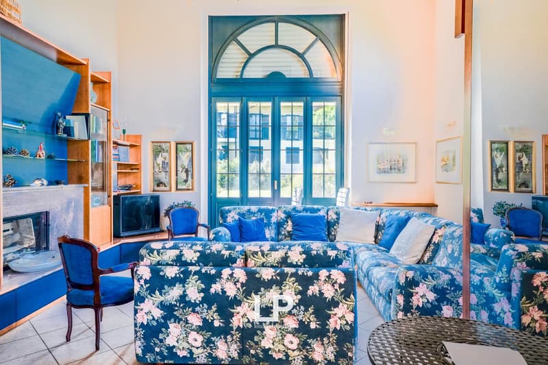 Spacious living room with large arched windows, blue floral patterned sofa and chairs, wooden shelving unit, and a fireplace