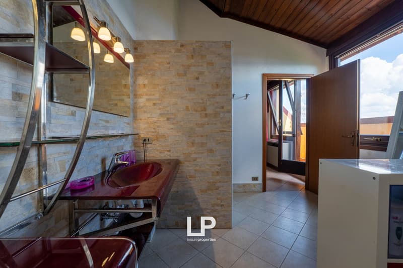 Bathroom with stone tile walls, vanity with red countertop, and glass shower enclosure. Open doorway leading to another room.