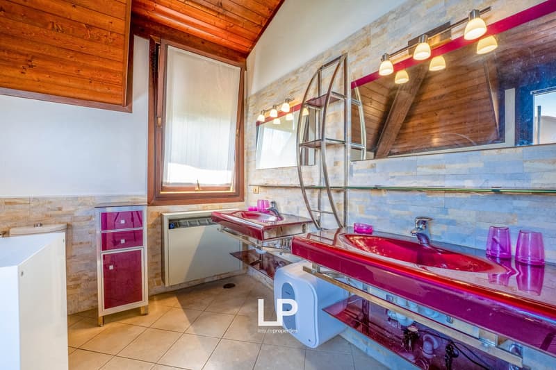 Spacious bathroom with wooden ceiling, stone walls, modern vanity with red countertop, shelving, and a dishwasher