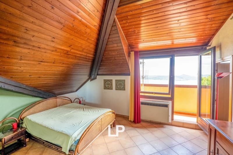 Spacious bedroom with wooden ceiling and walls, large windows providing a scenic view, rattan furniture, and a balcony or terrace access.
