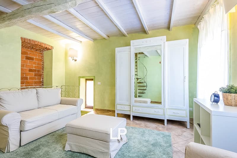 Spacious living room with exposed brick fireplace, white sofa and armchair, wooden ceiling beams, and a large white wardrobe cabinet