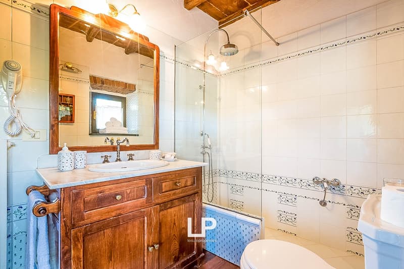 Wooden vanity with drawers, large mirror, tiled walls, shower enclosure, wooden ceiling beams