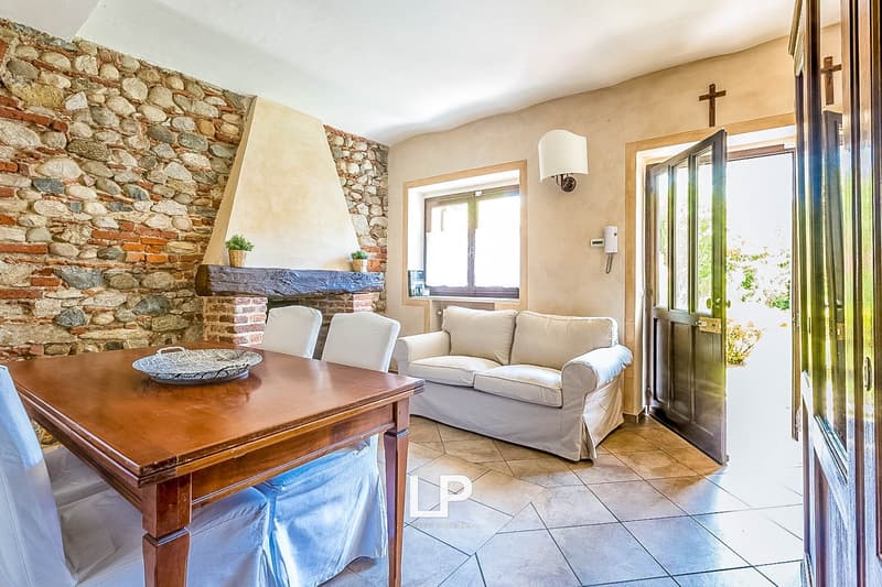 Rustic living room with stone wall, wooden dining table, sofa, and sliding glass doors leading to an outdoor area