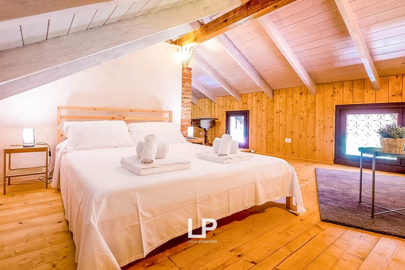 Spacious bedroom with wooden walls and ceiling, large bed with white bedding, wooden furniture, and a fireplace