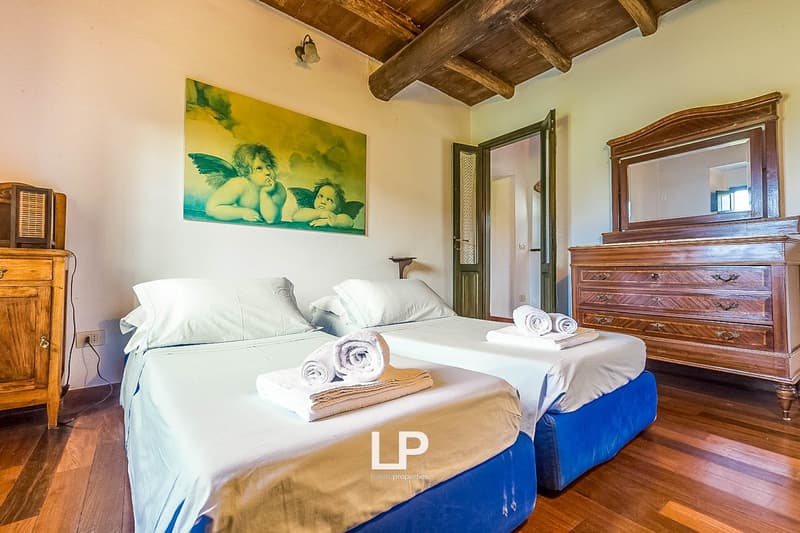 Spacious bedroom with wooden beamed ceiling, large bed with white linens, wooden dresser, and a painting of cherubs on the wall
