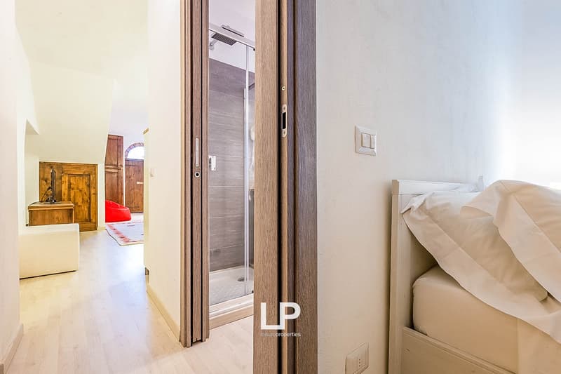Bedroom with wooden doors, glass shower enclosure, and a bed with white bedding