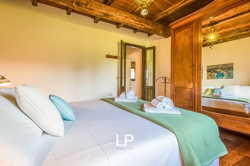 Rustic bedroom with wooden beamed ceiling, wooden furniture, white bedding, green blanket, and artwork on the wall