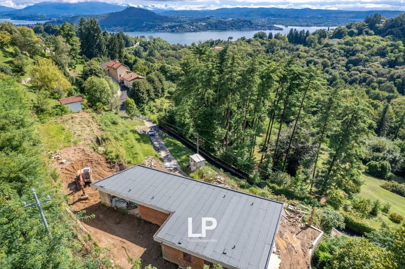 Under construction modern house, concrete roof, surrounded by greenery, partial view of a lake