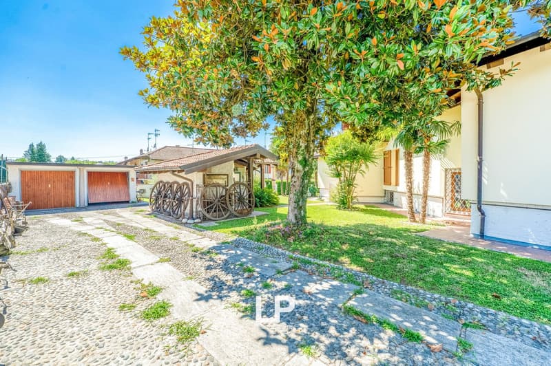Detached house, brick wall, driveway with stone tiles, wooden garage doors, large tree, lawn, wheel carts