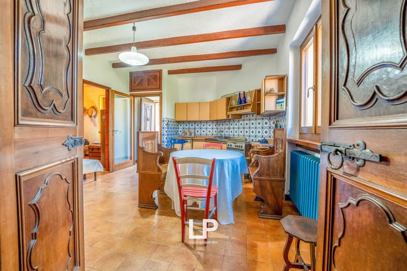 Traditional house, tile flooring, vintage style kitchen, dining area with table and chairs, wooden beams on ceiling, blue tile backsplash, wooden doors