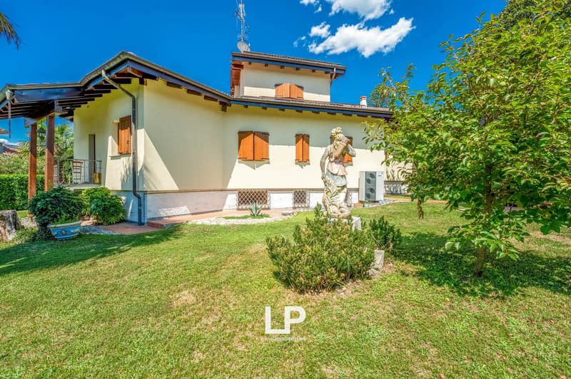two-story house, beige exterior, brown wooden shutters, terracotta roof, statue, lush green garden, patio, trees, well-maintained