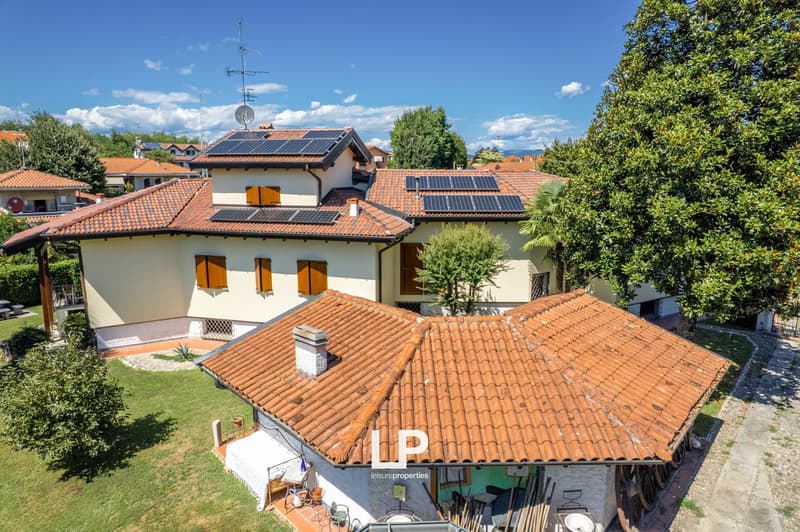 2-story house, red roof tiles, solar panels on the roof, patio, trees, and greenery in the yard