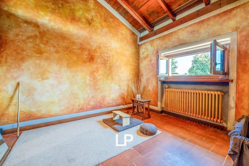 Orange wall painting, wooden floor, white carpet, small wooden table, open window with a view, orange radiator, stick and cushion on the floor.