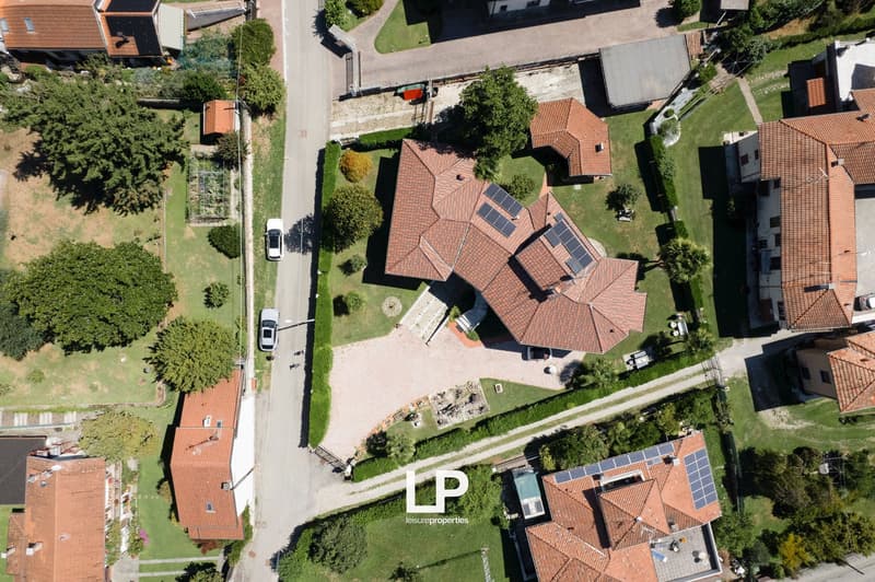 House with solar panels on roof, red tiled roof, driveway, multiple buildings, landscaped garden, surrounding houses.