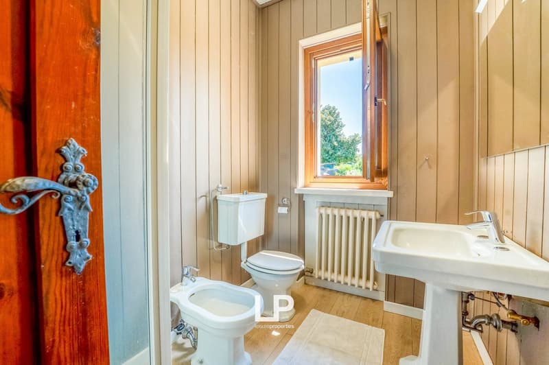 wooden walls, white toilet and bidet, white pedestal sink, radiator, window with view of outside