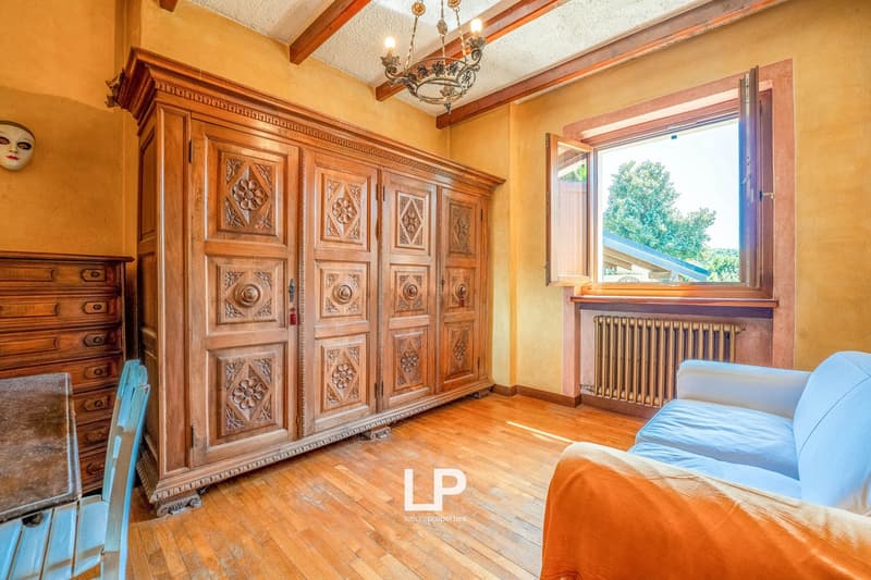 Hardwood floor, yellow walls, wooden wardrobe, large window, white couch, wooden chair, chandelier, radiator, face mask on wall