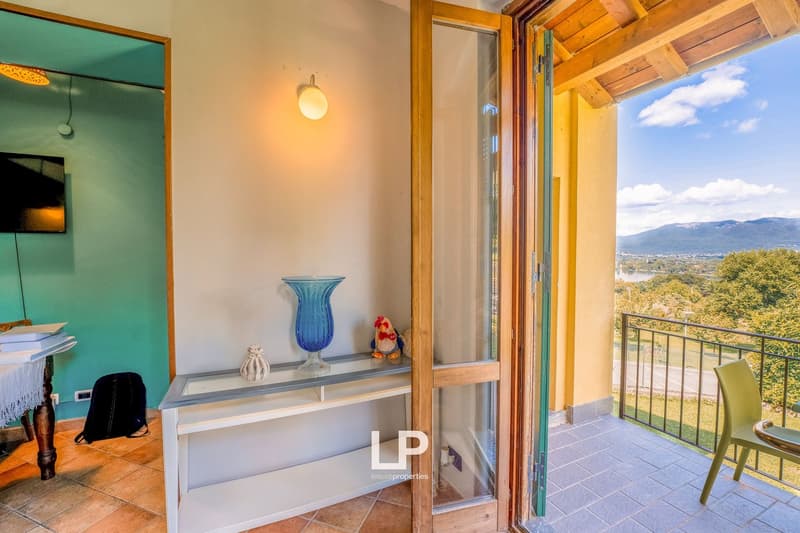 wooden door leading to balcony, balcony with view of greenery, chair, shelf with vase, books on desk, green wall with TV
