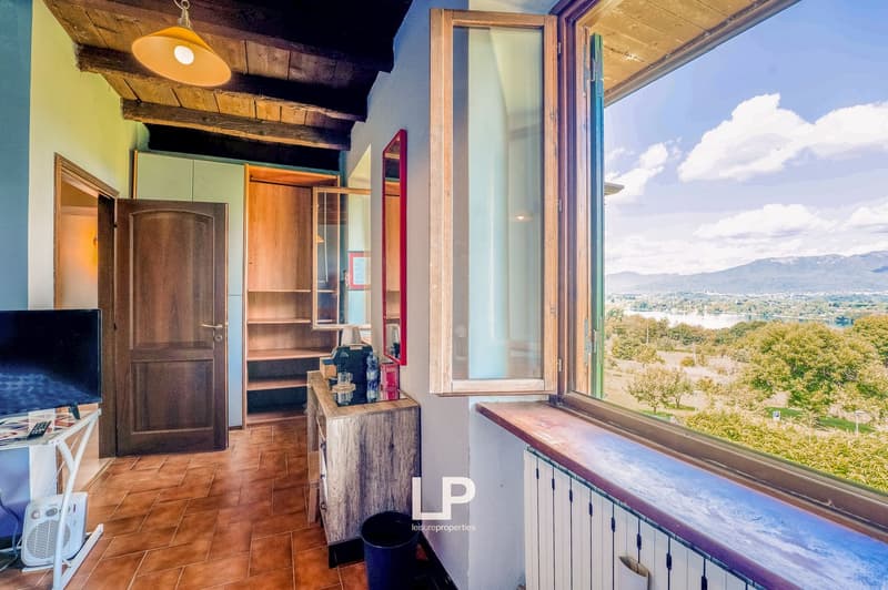 open door, wooden wardrobe, mirror, large window with view, tiled floor, desk with monitor and remote control, radiator, trash bin